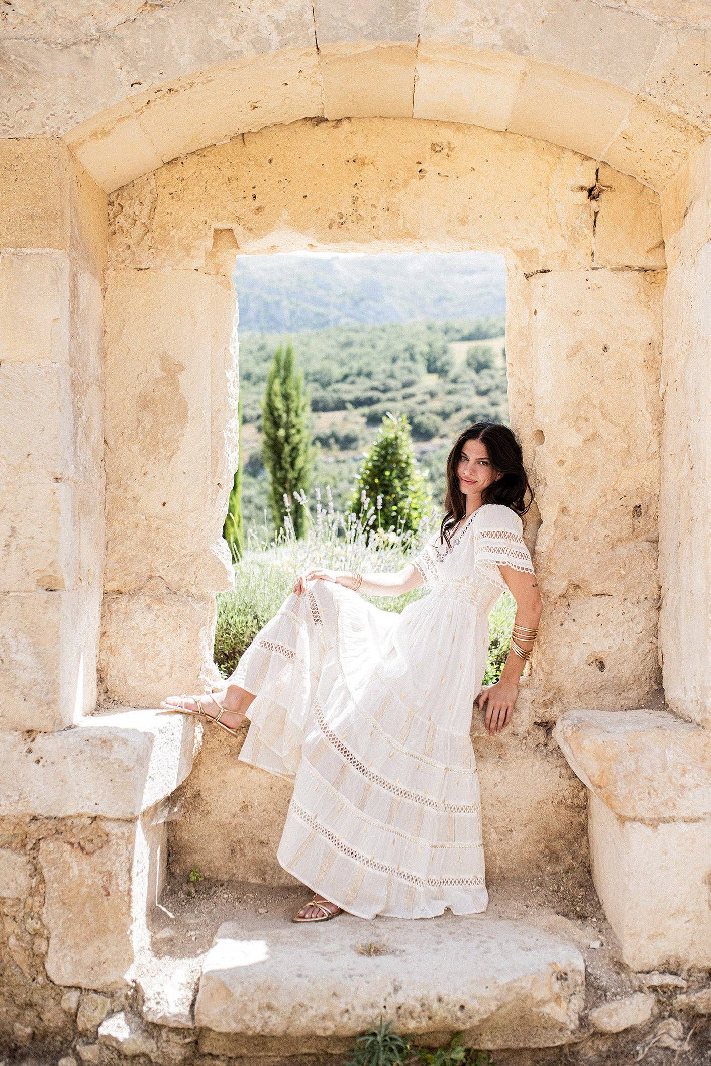 Boho-Kleid aus Baumwolle in Off-White mit goldenen Details – Model trägt das Martinique Kleid im mediterranen Setting