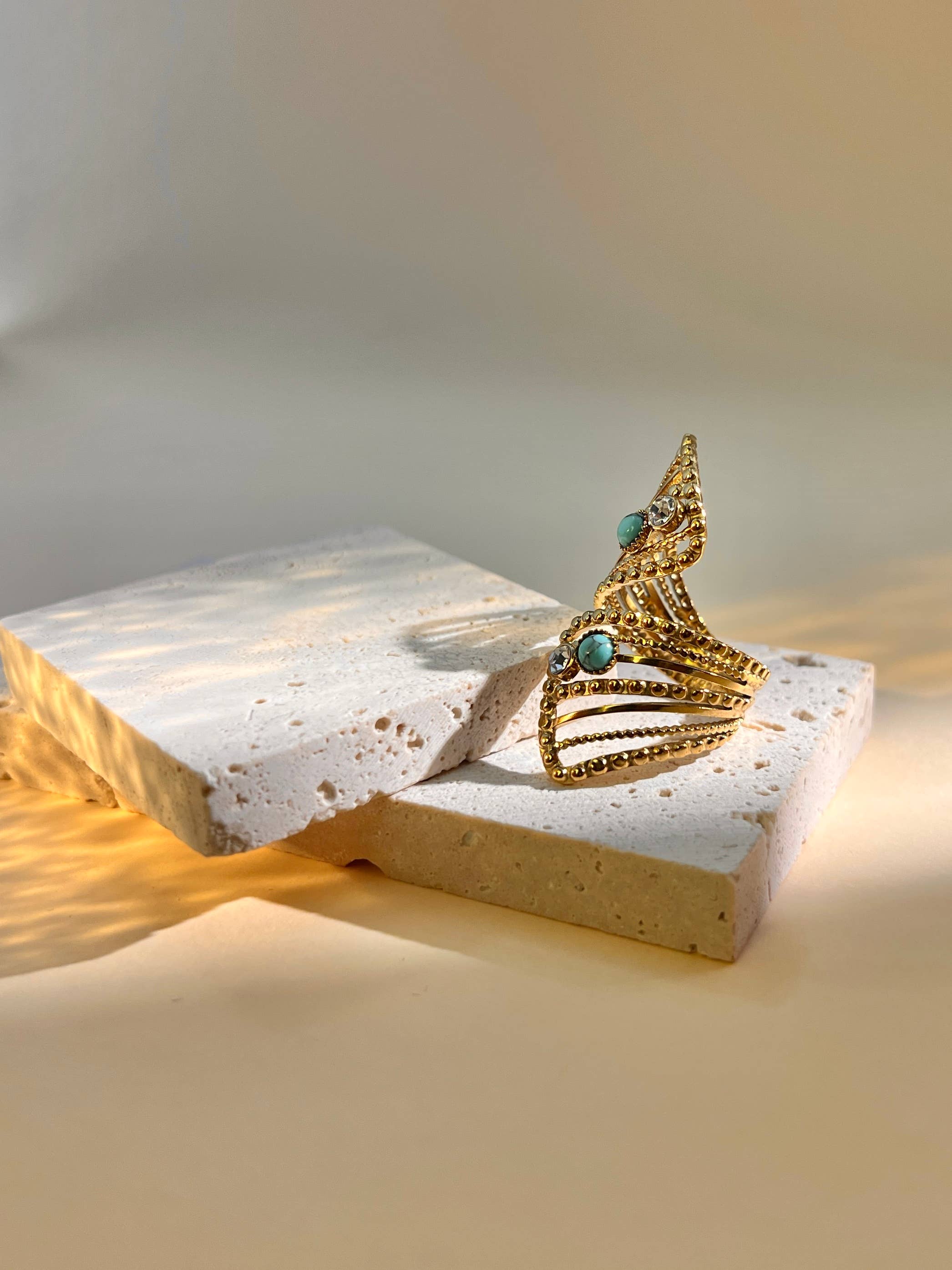 Goldener Ring mit offenem Design und türkisfarbenen sowie klaren Steinen auf hellem Untergrund