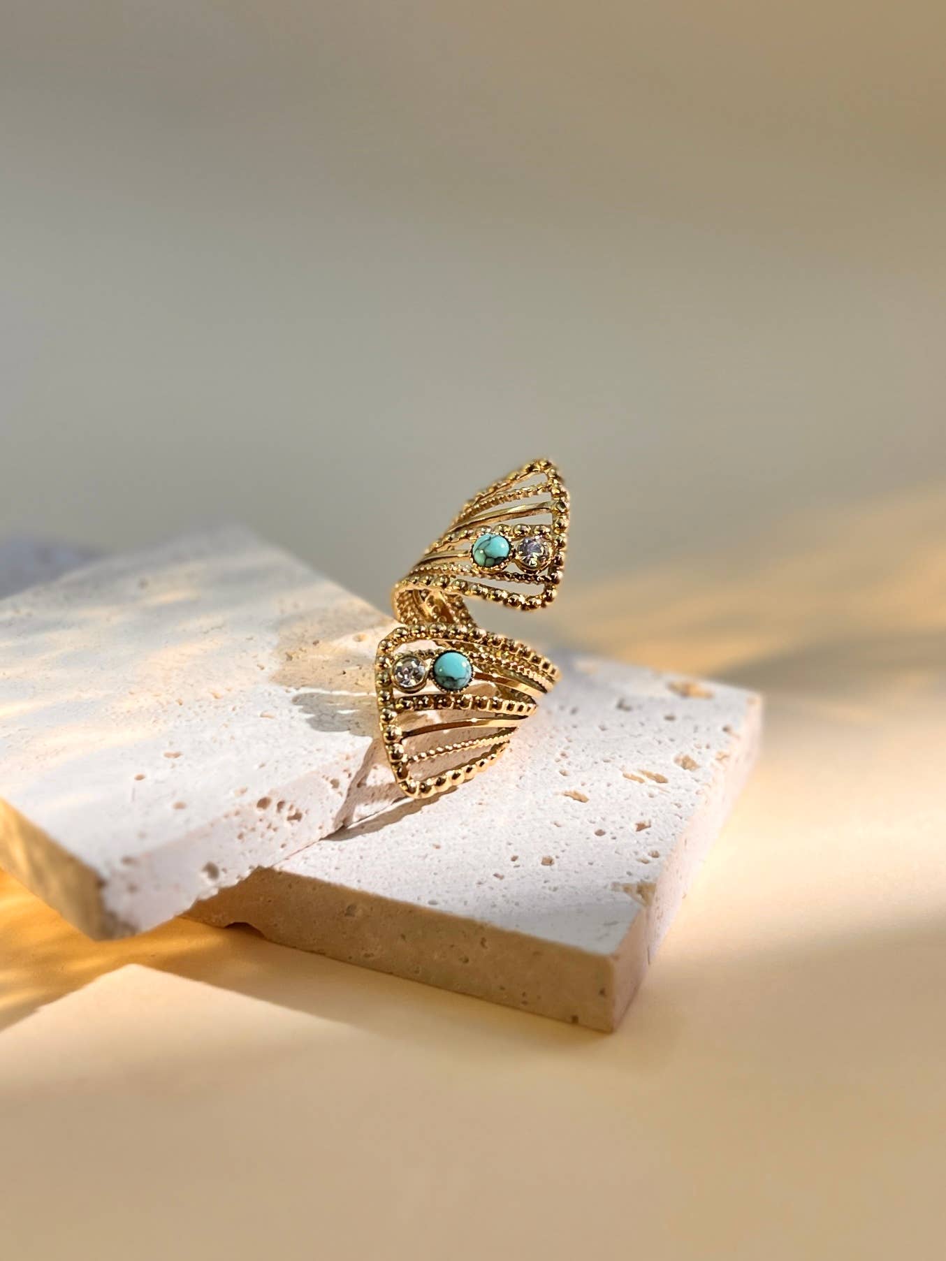Goldener Ring mit offenem Design und türkisfarbenen sowie klaren Steinen auf hellem Untergrund