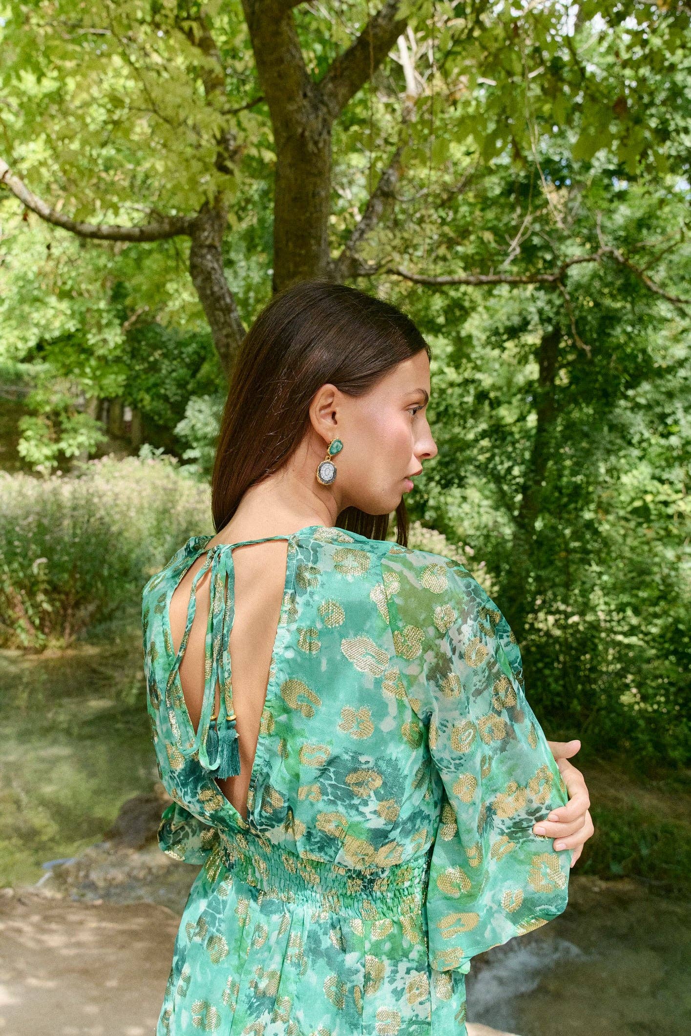 Model trägt Jumpsuit „Kenia“ mit Rückenausschnitt in grüner Naturkulisse