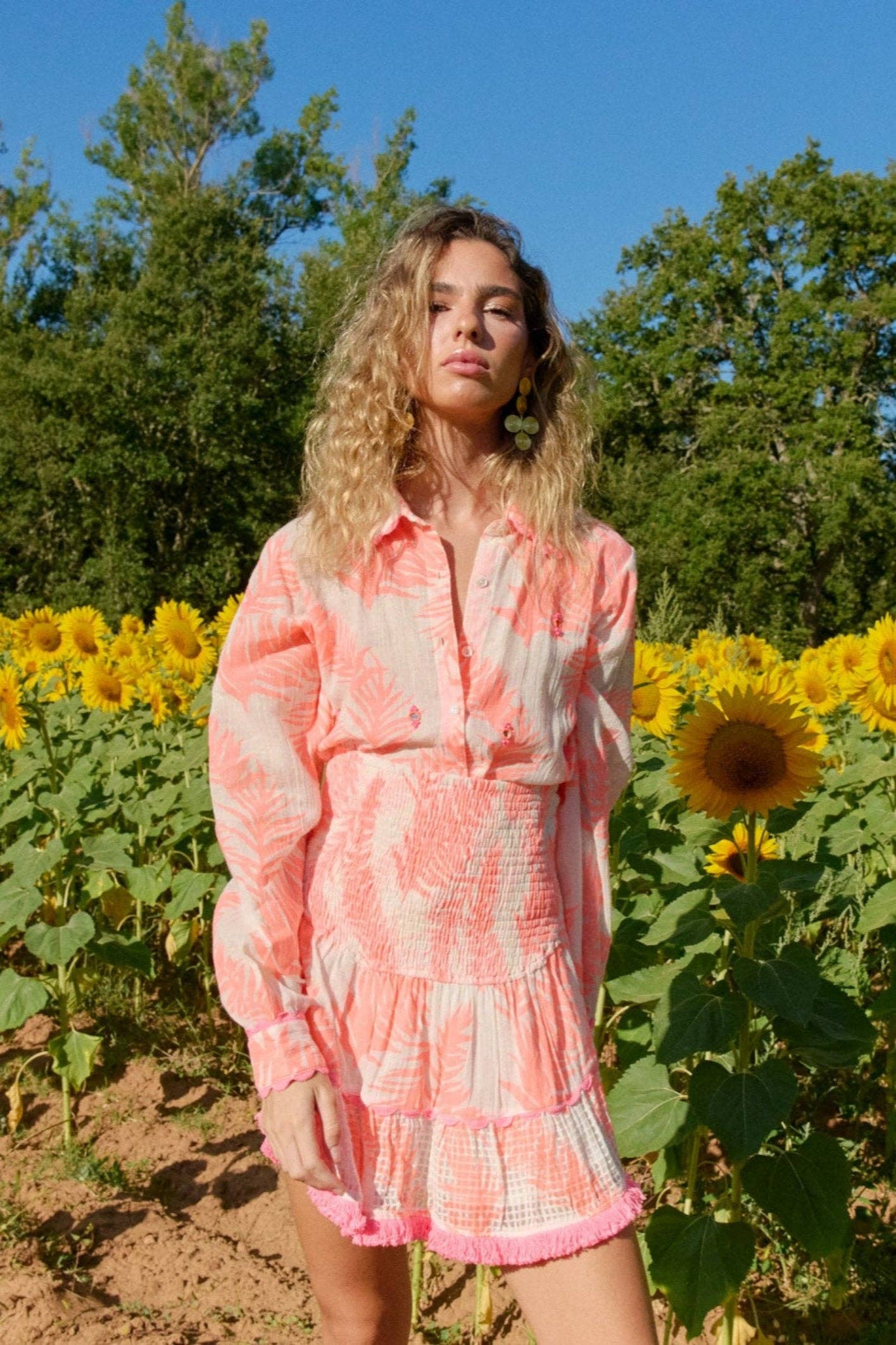 Model trägt das Shirt „Nilo Neon Orange“ vor einem Sonnenblumenfeld – Frontansicht mit langen Ärmeln