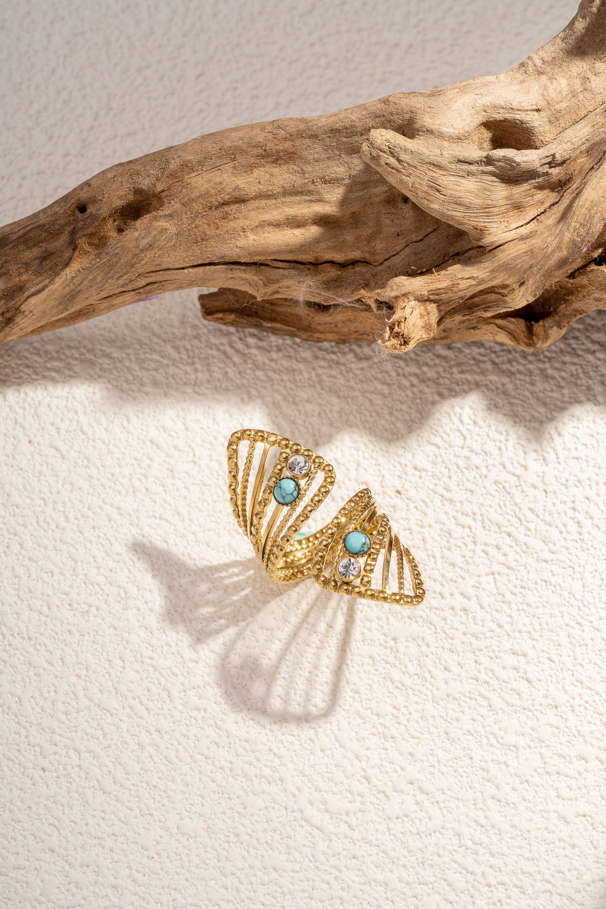 Goldener Ring mit offenem Design und türkisfarbenen sowie klaren Steinen auf hellem Untergrund