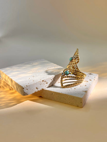 Goldener Ring mit offenem Design und türkisfarbenen sowie klaren Steinen auf hellem Untergrund