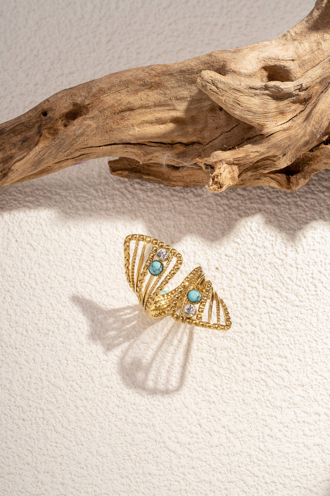 Goldener Ring mit offenem Design und türkisfarbenen sowie klaren Steinen auf hellem Untergrund