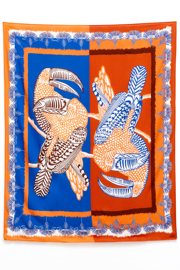 Produktfoto: flach gelegter Pareo mit Papageien auf Blau-Orange-Hintergrund.
